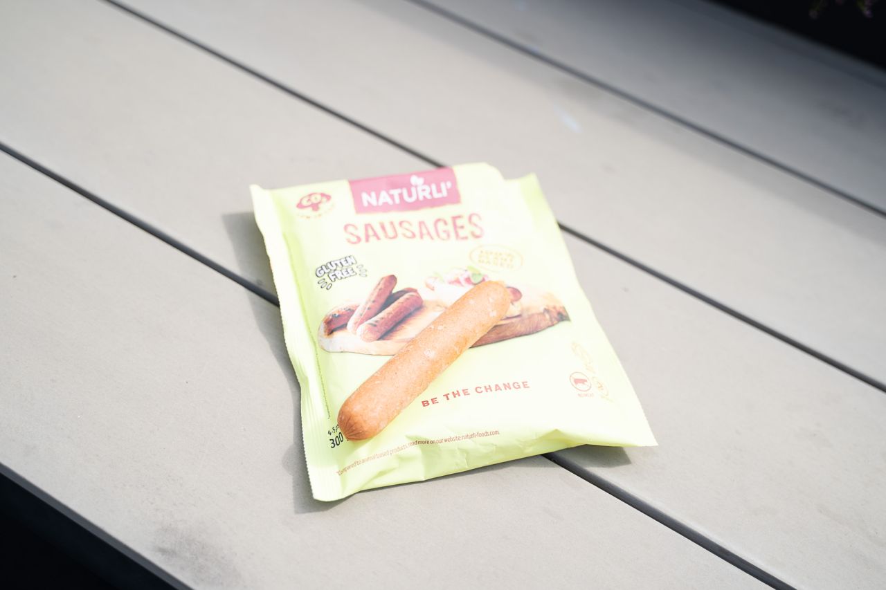 Naturli's plantebaserede pølser kan blandt andet handles i Bilka, Meny og på Nemlig.com. Foto: Thomas Schønning Gullig pose med veganske grillpølser, hvor én af pølserne er taget ud og lagt ovenpå.