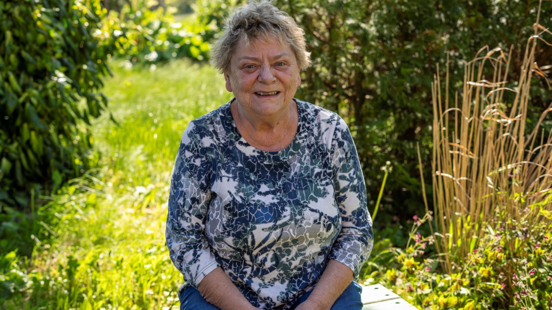 Kirsten Sørensen siddende på en bænk i sin skønne, vilde have. Foto: Dyrenes Beskyttelse